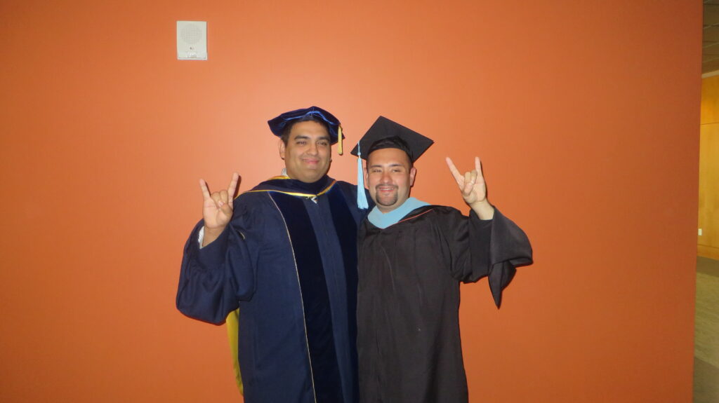 Jose and Dr. Victor Saenz (left) raise their horns on graduation day