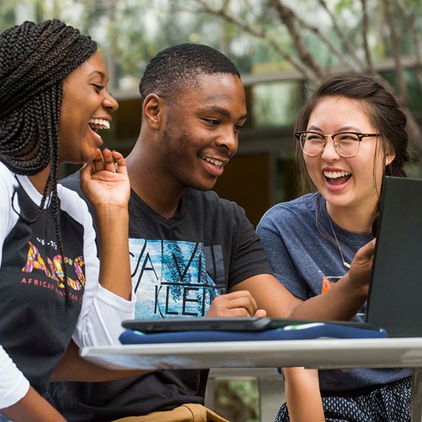 A group of UT Austin students laughing while working on a laptop computer